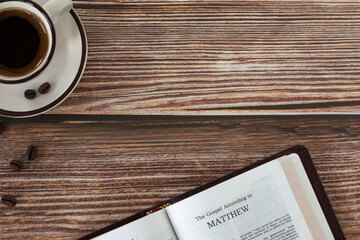 Open holy bible book Matthew gospel with coffee cup on wooden background. Copy space. Top table...