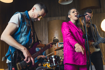 a singer woman in pink clothes standing in front of guitarists and a drummer playing in the...