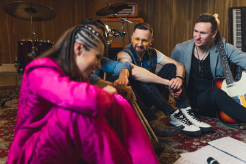 two guitarists, a drummer and a singer on the floor discussing about their new song in the studio....