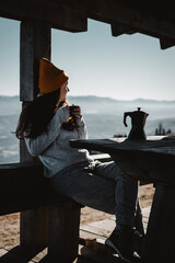 Woman with cup of coffee is sitting in front of mountain view and look away