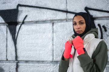 Portrait of young muslim woman with sports gloves, standing in front of graffiti.