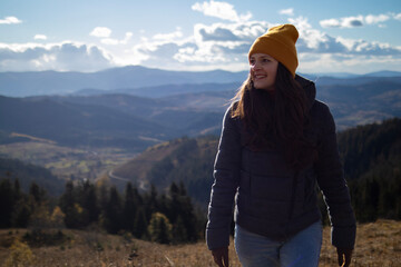 Fototapeta na wymiar Young happy woman in orange beanie is walking in front of mountains landscape