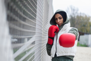 Portrait of young muslim woman with boxing gloves standing outdoor in city.