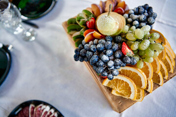 Catering. buffet. Fruit wooden plate. Grapes, kiwi, oranges, peach, strawberries. Table setting.