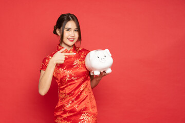 Fototapeta na wymiar Asian woman wearing red traditional cheongsam qipao dress showing and holding piggy bank isolated on red background, Business and financial concept
