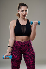 Plus size woman working out with dumbbells on gray