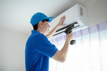 An Asian young Technician service man wearing blue uniform checking ,  cleaning air conditioner in home