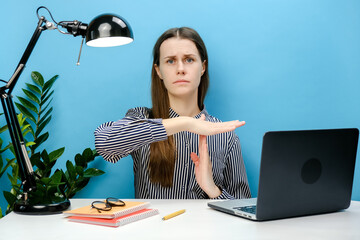 Strict employee young business woman 20s in shirt sitting work at white office desk with laptop holding stop gesture hands perpendicularly, posing isolated over blue color background wall in studio - obrazy, fototapety, plakaty