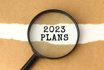 The magnifying glass reveals the 2023 PLANS text appearing behind the torn brown paper.