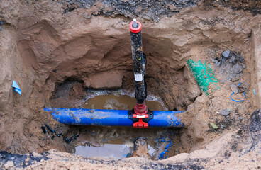 Blick auf einen freigelegten Wasseranschluss mit Ventilen, Rohren und Leitungen in einer Baugrube,...