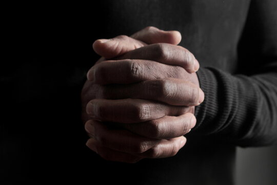 man praying to god with hands together Caribbean man praying with black background stock photo