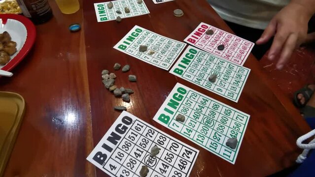 Unidentifiable people playing classic bingo card games on a shiny brown table. High angle close up
