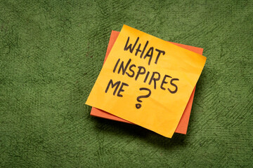 What inspires me? Handwritten question on a sticky note. Inspiration and personal development concept.