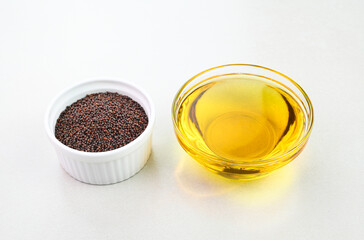Mustard seed oil in a glass cup with mustard seeds in a bowl.