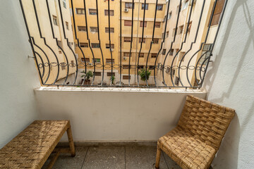 Two rattan chairs in an empty balcony with a view over residential buildings