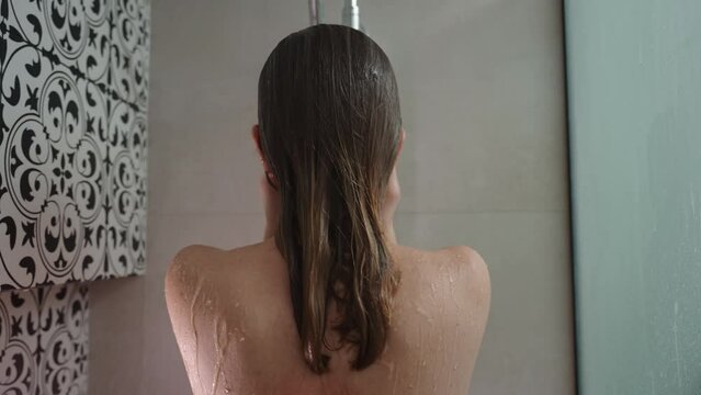 Back view of naked woman taking shower in shower stall. Woman washing her hairs in bathroom. Morning hygiene