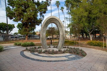 a tall concrete arch sculpture in a gorgeous autumn landscape at Lincoln Park with lush green trees, grass and plants and blue sky with clouds in Los Angeles USA