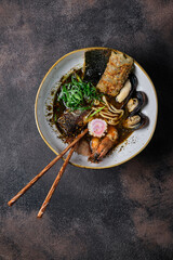 Asian style soup with udon noodles, pork, shrimp, mussel and green onions on dark background