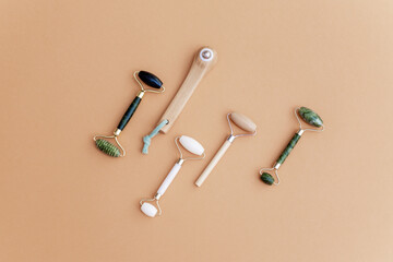 Various facial massage rollers for facial massage on a beige background. Natural wooden and jade...
