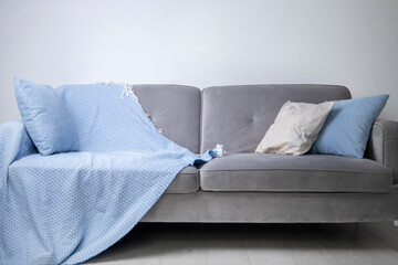 On a gray sofa lies a blue bedspread and decorative pillows against a white wall