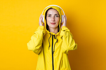 Young woman in headphones in a yellow jacket on a yellow background.