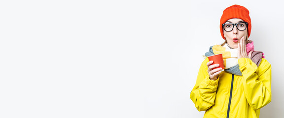 Surprised young woman with a paper cup on a light background. Banner.