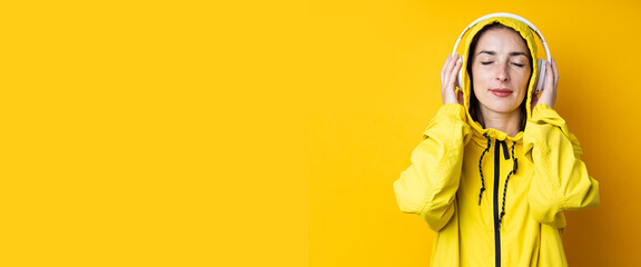 Young woman in headphones listening to music with closed eyes on yellow background. Banner.