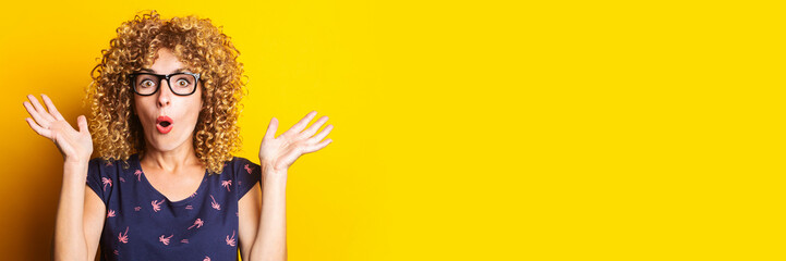 shocked surprised curly young woman with glasses on a yellow background. Banner