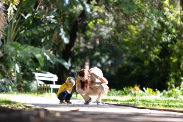 A woman with her little blond son walking in the park and looking down at the path