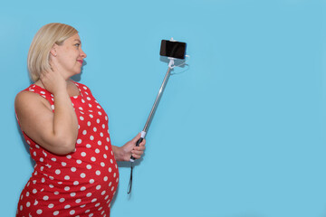 pregnant woman taking selfie on blue background with copy space