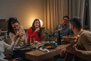Group of friends having a dinner party and playing classical guitar