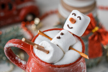 Marshmallow snowman taking hot tub in a red ceramic cup full of cocoa with milk foam. Christmas holidays layout. Wintertime concept. Hot chocolate with marshmallow and festive decoration.
