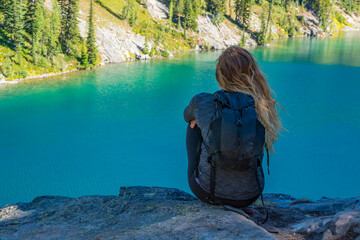 Adventurous athletic woman sitting on a hill overlooking an alpine lake on a beautiful sunny day in the Pacific Northwest.
