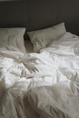 Bedroom concept. Comfortable bed with white crumpled bed linens, pillows. Sunlight shadow reflections. Morning in bed