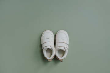 White mini sneaker shoes. Baby shoes on soft pastel green background. Fashion Scandinavian children's clothes. Flat lay, top view