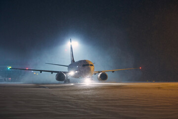 Fototapeta na wymiar Winter night at airport. Airplane taxiing to runway for take off during heavy snowfall..