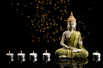 Buddha statue in meditation with lights and candles on black background with copy space.