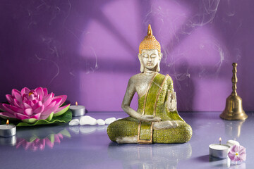Green and golden buddha statue in meditation on light purple background with copy space.