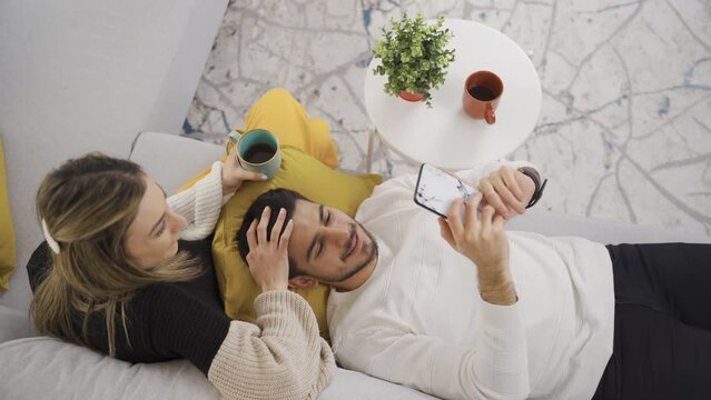 Young couple hugging each other, talking while relaxing on sofa in modern home.
Young couple talking while relaxing on sofa at home, sharing dreams, dreaming together, enjoying romantic day.
