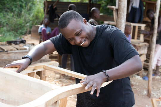Young African carpenter searching and choosing wood and using sandpaper to rub the wooden plank at workshop table in carpenter factory