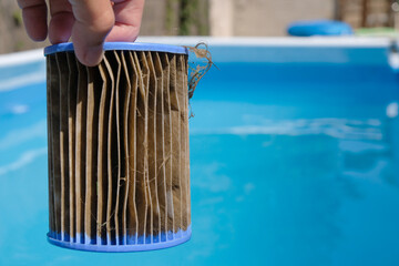 Dirty Replacement Pool Filter Cartridge in a woman's hand on the pool background. Substances that...