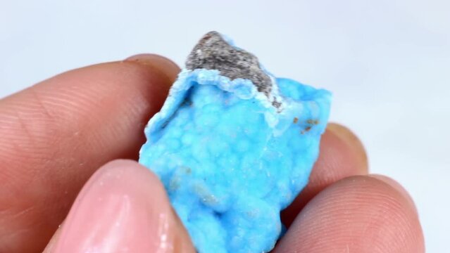 Woman hand holding bright light blue crystal Turquoise on light background close up