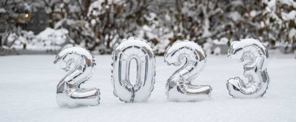 Banner with silver numbers of the New Year 2023 in winter in the snow on the background of snow-covered trees and bushes with copy space