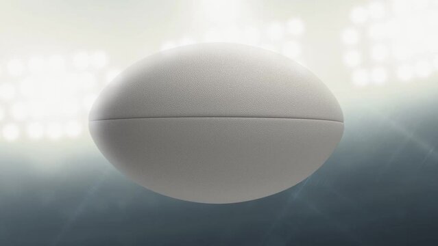 A seamlessly loop able animation of a white textured rugby ball spinning and rotating on floodlit stadium background in the night time