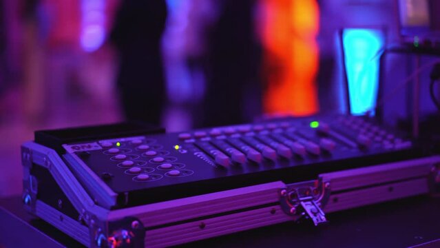 Blinking neon disco lights at nightclub, blurred people dancing in the hall, close up shot of dj mixing controller with different buttons and sliders for sound regulation