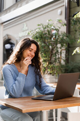 Confident business woman is chatting using laptop with colleagues via video connection and discussing new ideas. Happy girl with laptop is chatting with her friends and family outdoor in cafe.