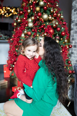 Fototapeta na wymiar Young woman kissing her cute daughter and celebrating Christmas at home