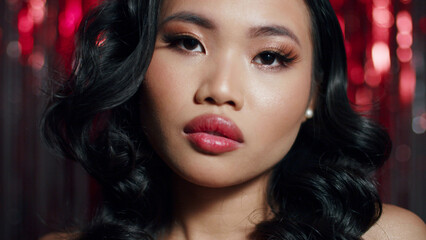 Alluring glamour asian woman with sensual look posing to a camera over red shiny background.