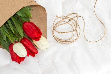 bouquet of tulips and phone black screen heart shape from sack rope or white cappuccino latte coffee eco cup with plastic cover on bedroom white blanket morning surprise gift valentines day march 8th 