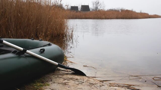 An inflatable boat with lowered oars stands on the sandy shore of the lake near the water in late autumn. Walks in the wild in late autumn